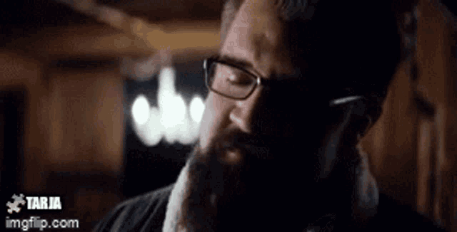 a man with a beard and glasses is making a funny face in a dark room .
