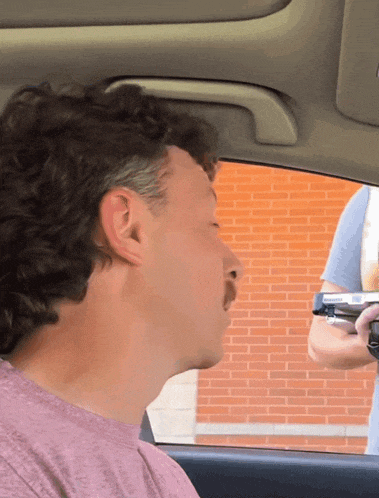 a man in a pink shirt is sitting in a car with his eyes closed