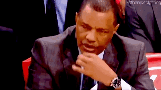 a man in a suit and tie is sitting in a stadium and covering his mouth with his hand .