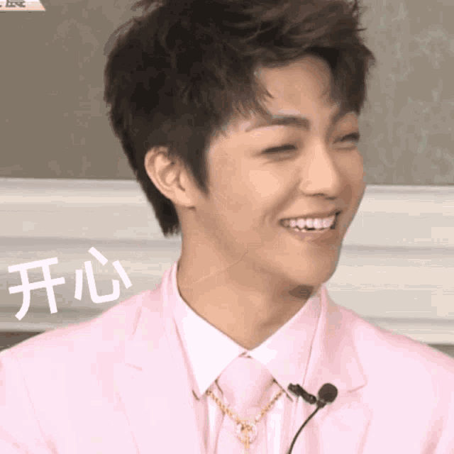 a man wearing a pink suit and tie smiles with chinese characters behind him