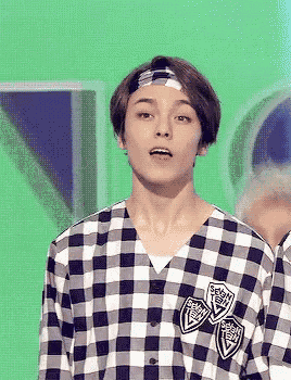 a young man wearing a headband and a plaid shirt is standing in front of a green background .