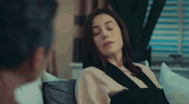 a woman with a broken arm is laying on a couch looking at a man .
