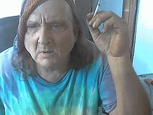 a man with long hair is wearing a tie dye shirt and holding a pen