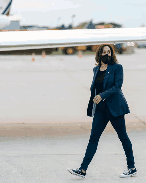 a woman wearing a mask and converse shoes walks on an airport tarmac