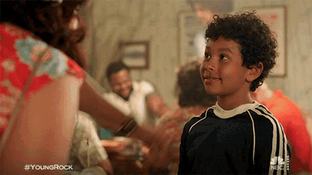 a young boy with curly hair is standing in front of a group of people with the hashtag #youngrock on the bottom right