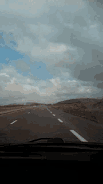 a car is driving down a highway with a cloudy sky