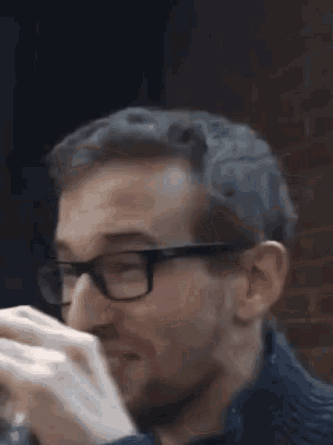a man wearing glasses is eating a sandwich