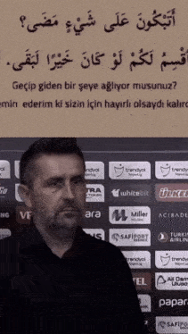 a man stands in front of a sign that says " gecip giden bir şeye agliyor musununuz "