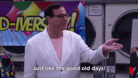 a man in a white suit and glasses is standing in front of a laundromat and says just like the good old days .