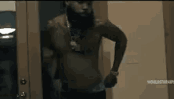 a shirtless man with a beard and a necklace is standing in a doorway .