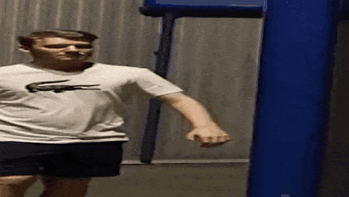 a man in a white shirt with a lacoste logo on it is standing next to a blue punching bag .