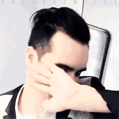 a man is covering his face with his hand while wearing a ring on his finger .
