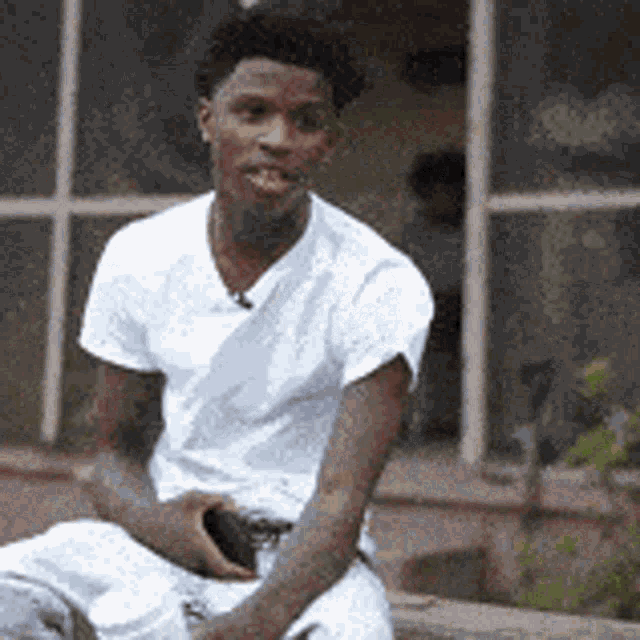 a young man in a white shirt is sitting on a porch holding a cell phone .