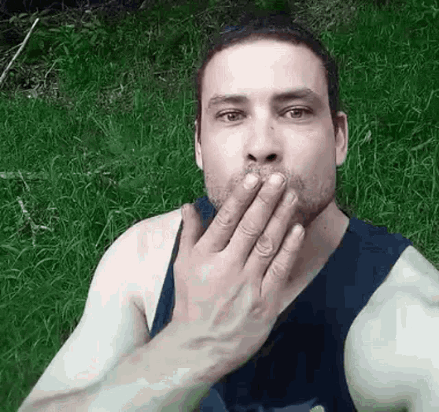 a man is covering his mouth with his hand while sitting on the grass .