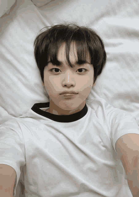 a young boy in a white shirt is laying on a bed and taking a selfie