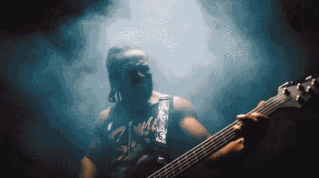 a man with dreadlocks is playing a guitar in a dark room with smoke behind him