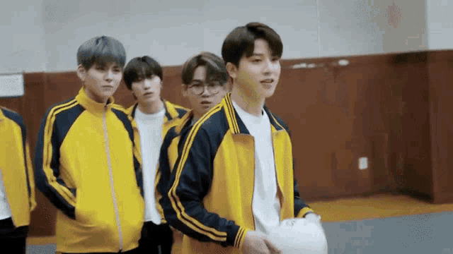 a group of young men are standing in a gym wearing yellow and blue jackets .