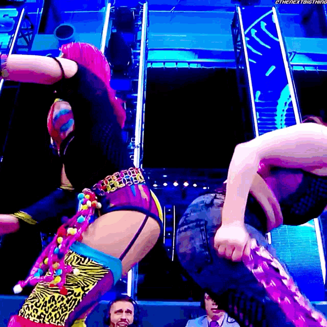 a couple of women are dancing in front of a sign that says ' the next thing ' on it