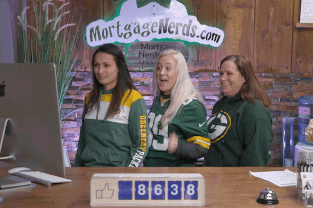 three women wearing green bay packers jerseys stand in front of a computer screen