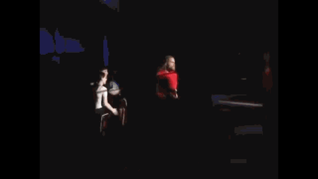 a wrestler in a red shirt is standing in a wrestling ring holding a rope .