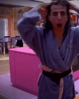 a woman in a blue robe is standing in front of a pink counter and holding her hair .