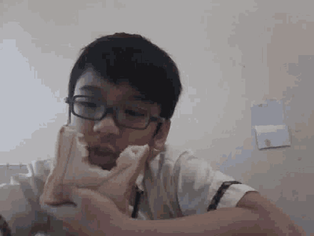 a boy wearing glasses is eating a piece of bread