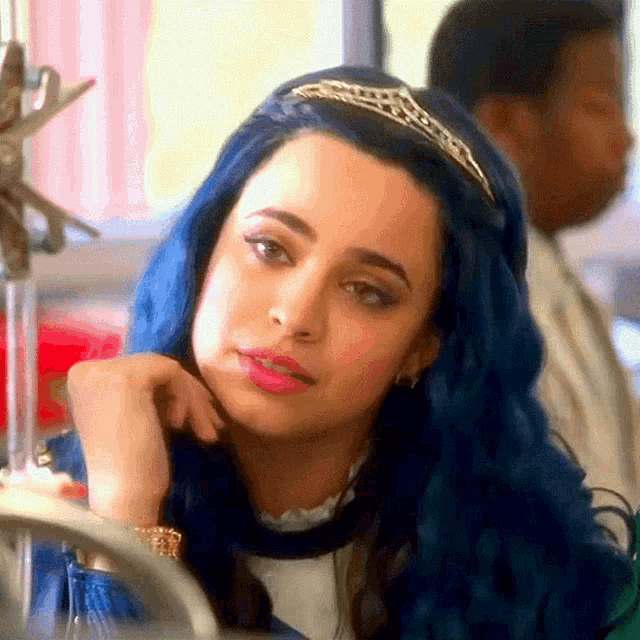 a woman with blue hair is wearing a tiara on her head .
