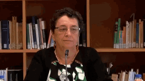 a woman sitting in front of a bookshelf with a microphone in front of her
