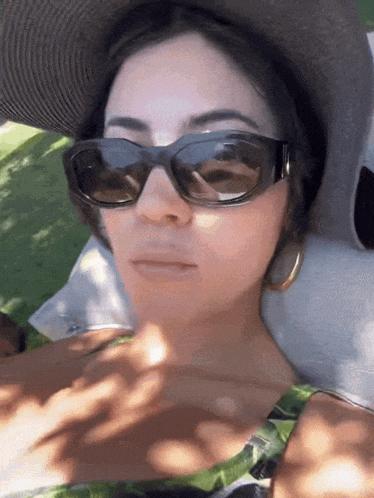 a woman wearing sunglasses and a hat is laying on a pillow