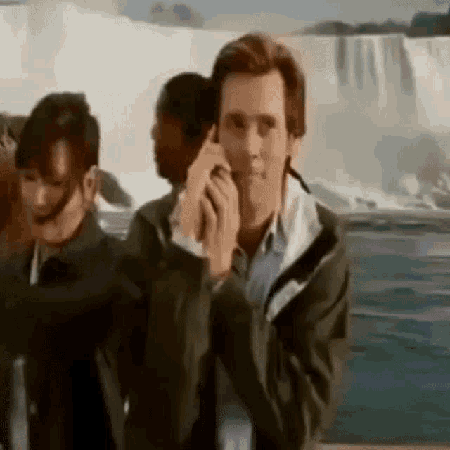 a man is talking on a cell phone in front of a waterfall while standing next to a group of people .