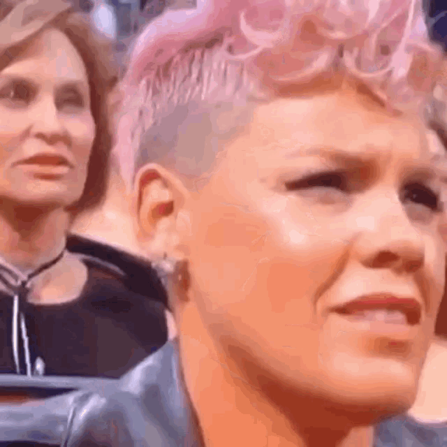 a close up of a woman 's face with pink hair and a shaved head .