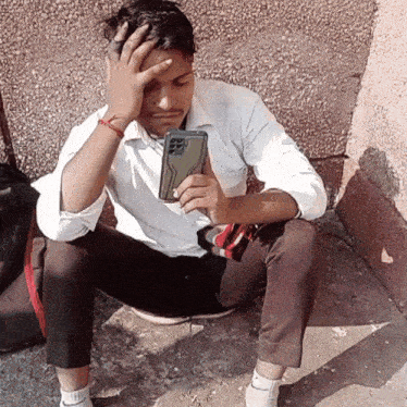 a man is sitting on the ground looking at his cell phone