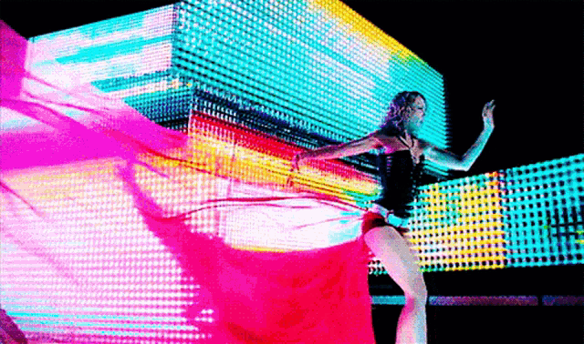 a woman in a red dress is dancing in front of a large screen of lights