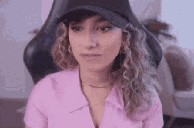 a woman in a pink shirt and black hat is sitting in a chair .
