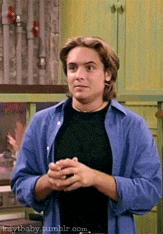 a man wearing a blue shirt and a black shirt is standing in a kitchen