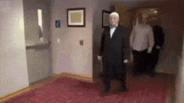 a man in a suit is walking down a hallway in front of a sign that says 2