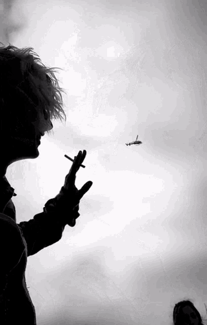 a silhouette of a person smoking a cigarette in front of a plane in the sky