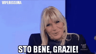 a woman with blonde hair is sitting in front of a blue background and says sto bene grazie !