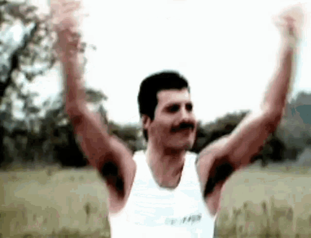 a man with a mustache is wearing a white tank top and raising his arms in the air .
