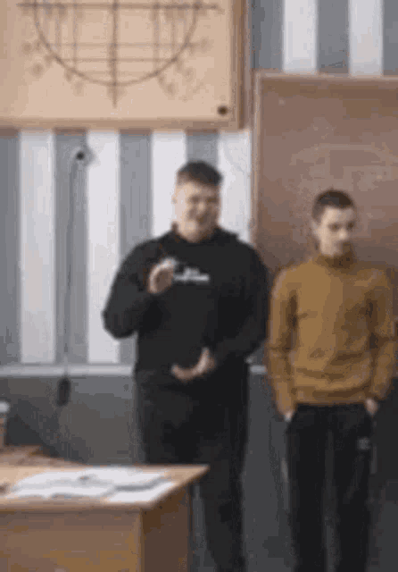 two men are standing in a classroom in front of a chalkboard .