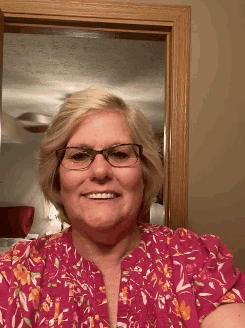 a woman wearing glasses and a pink top smiles for the camera
