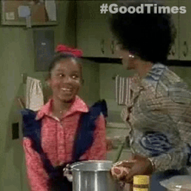 a woman and a girl are standing in a kitchen with a pot of food .