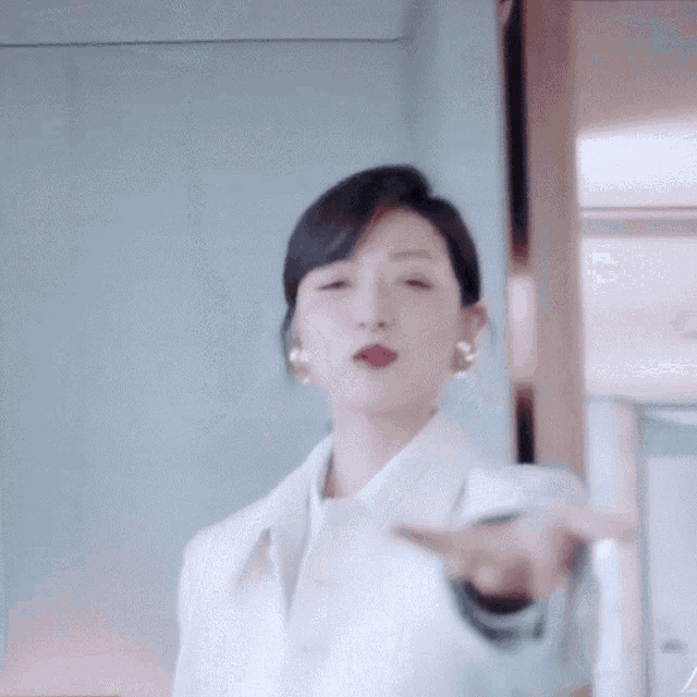 a woman in a white coat and earrings is pointing her finger