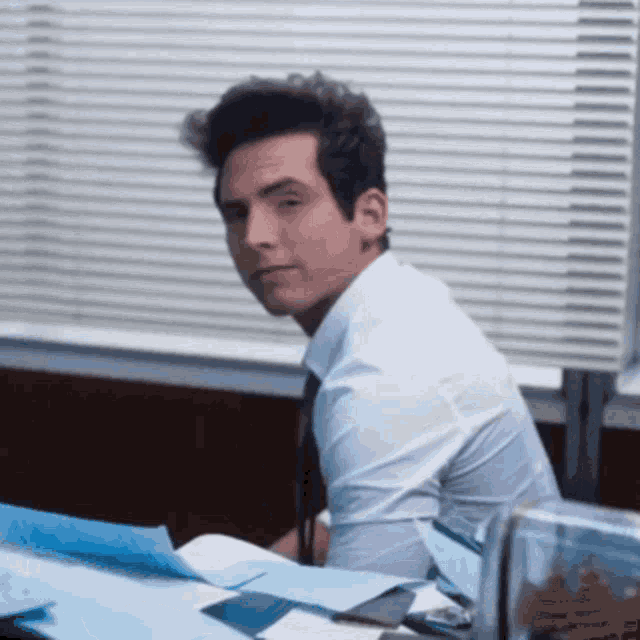 a man in a white shirt and tie is sitting at a desk in an office .