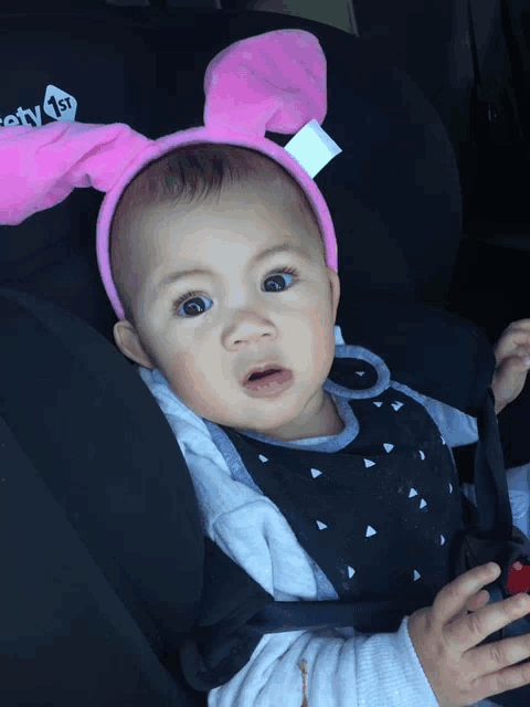a baby wearing bunny ears is sitting in a car seat