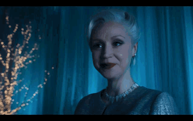 a woman with white hair and red lipstick stands in front of a blue background