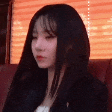 a young woman with long black hair is sitting on a red couch .