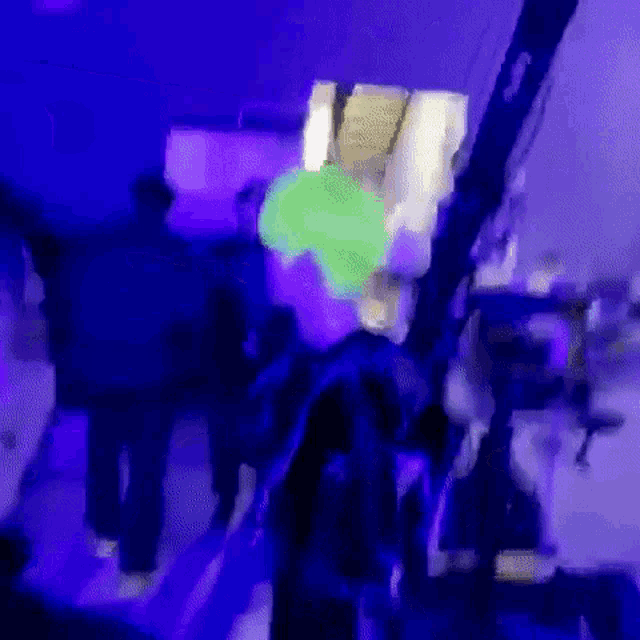 a group of people are dancing in a dark room with purple and blue lights .