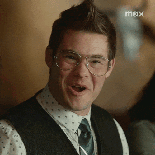 a man wearing glasses and a vest is making a funny face in front of a max logo