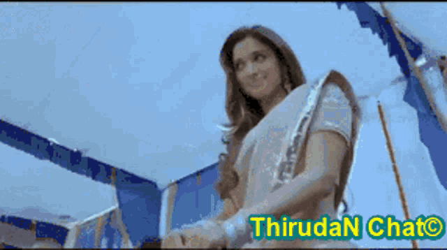 a woman in a white saree stands in front of a blue tent with the words thirudan chat on the bottom right